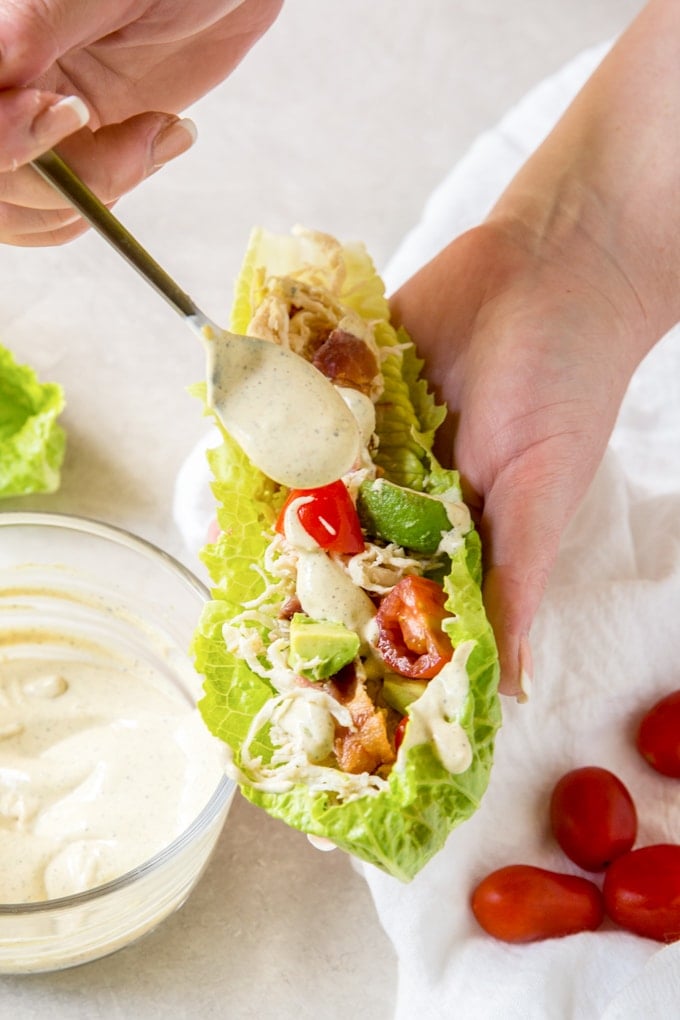 A hand holding a lettuce wrap and drizzling dressing on top