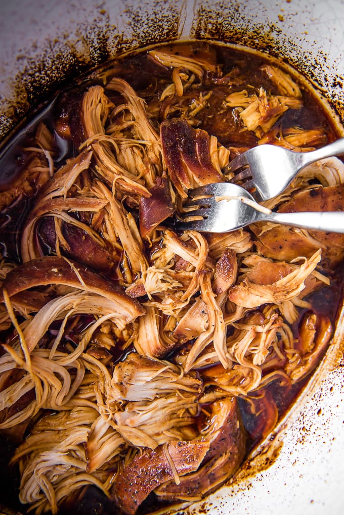 Shredded chicken in a slow cooker with barbecue sauce and two forks