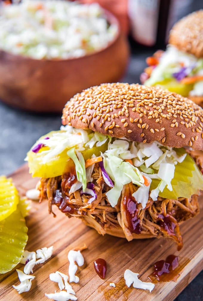 A bbq chicken sandwich topped with coleslaw and sliced pickles on a sesame seed bun