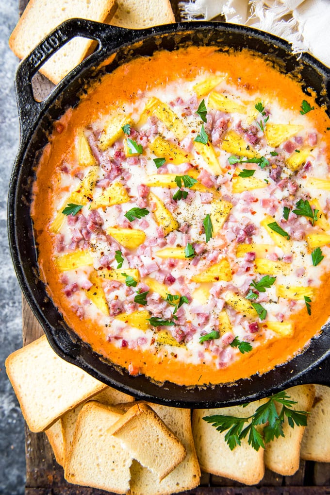 A cast iron skillet filled with hawaiian pizza dip and surrounded by toasted bread for dipping.