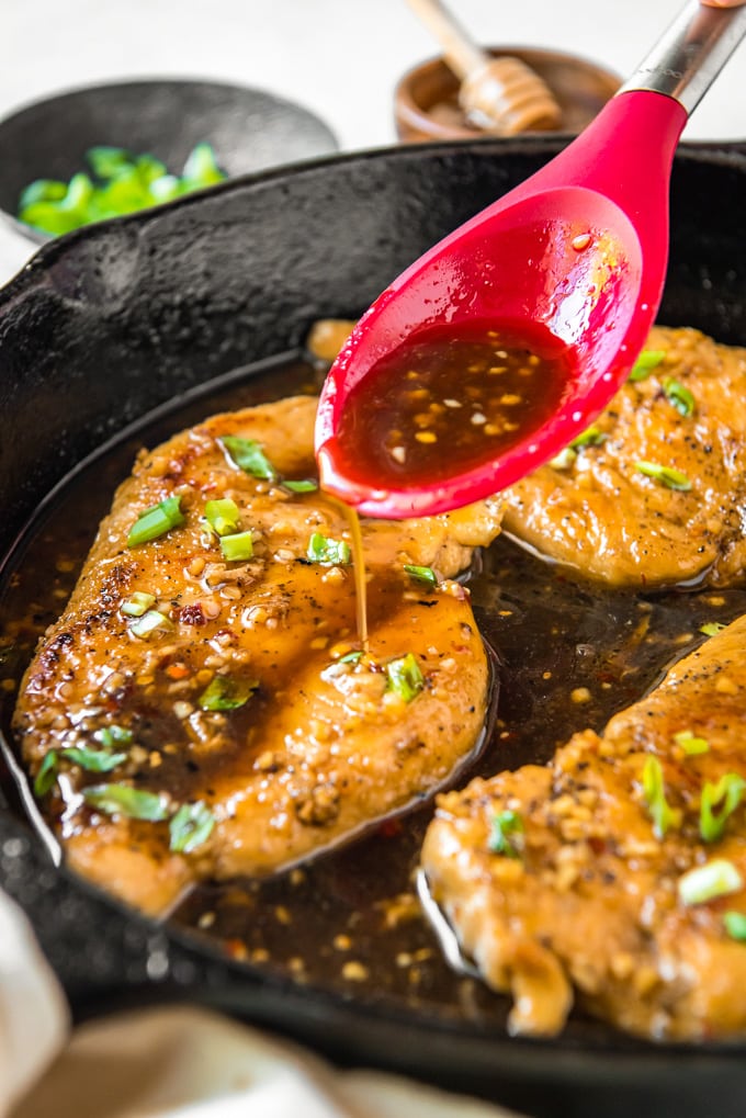 Honey garlic chicken in a skillet with sauce being poured on it.