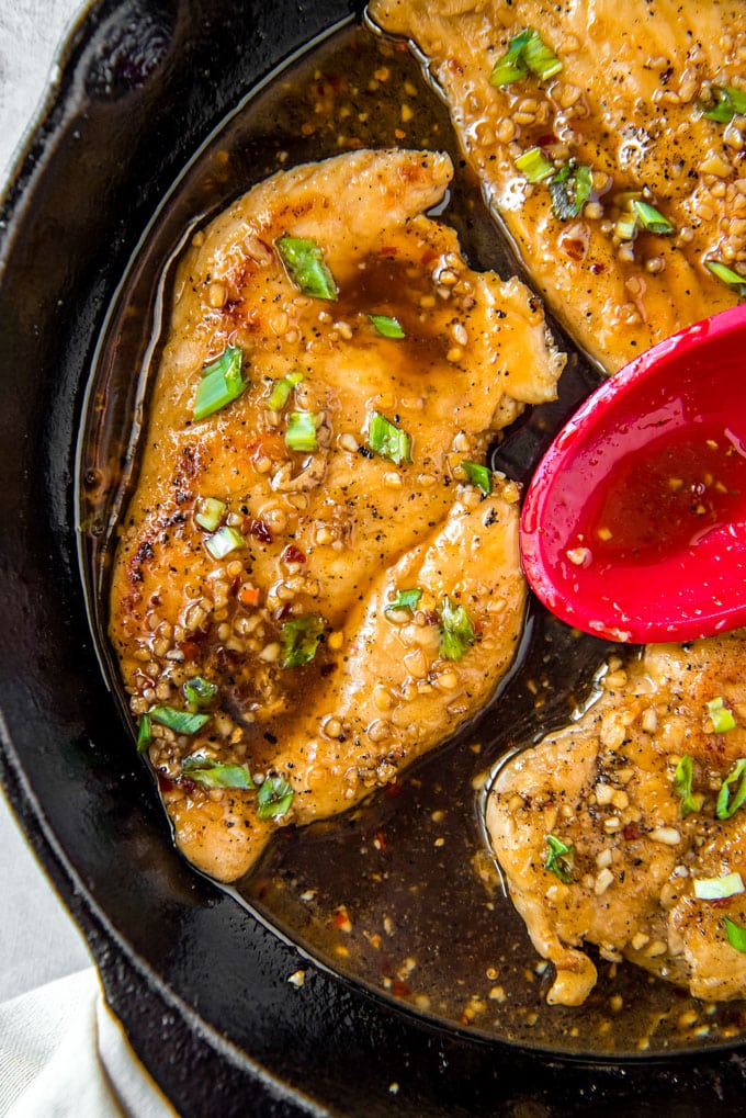 Honey garlic chicken in a cast iron skillet with a red spoon