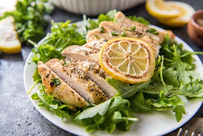 Lemon Pepper baked chicken sliced and sitting on a bed of arugula.