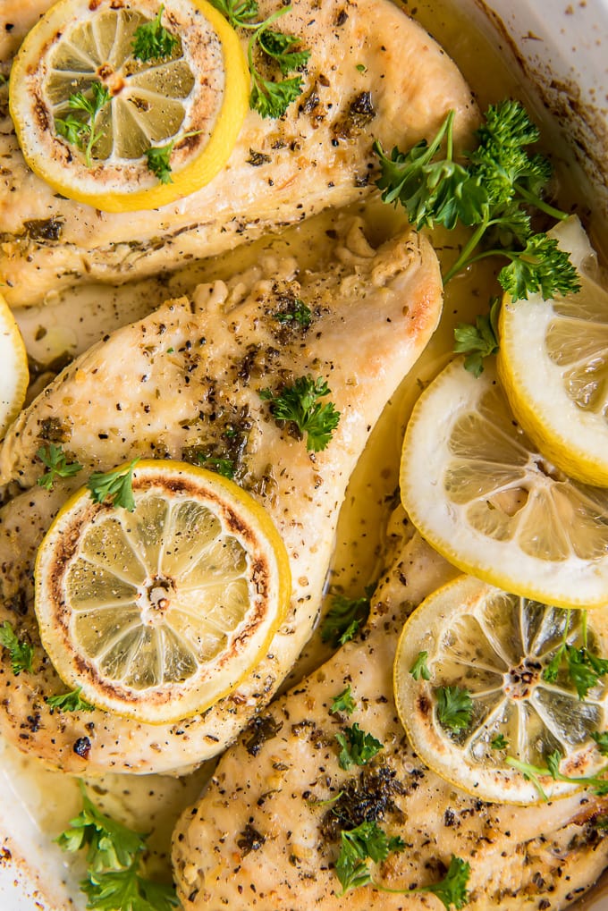 A close up of baked chicken breasts with lemon pepper seasoning and lemon slices.