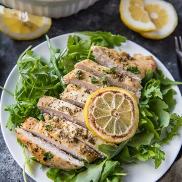 A bowl of salad on a plate, with Lemon and Chicken