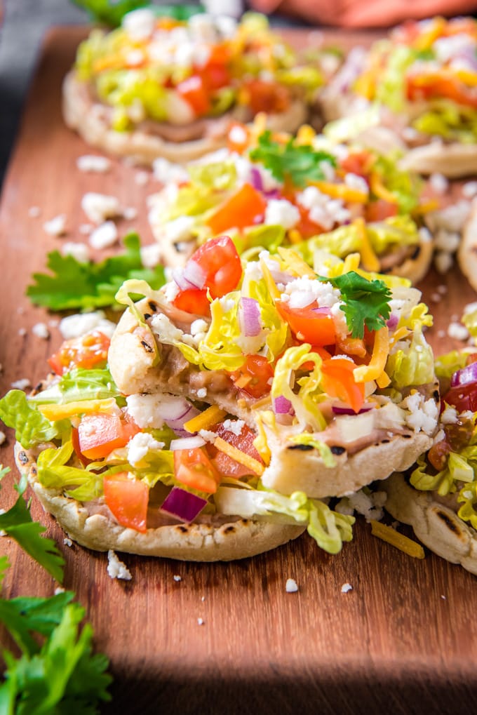 Authentic Sopes are a traditional Mexican dish that's perfect for Cinco de Mayo! Top them with beans, meat and vegetables for a delicious snack or meal. Mexican Sopes stacked, with a bit taken out of the top one