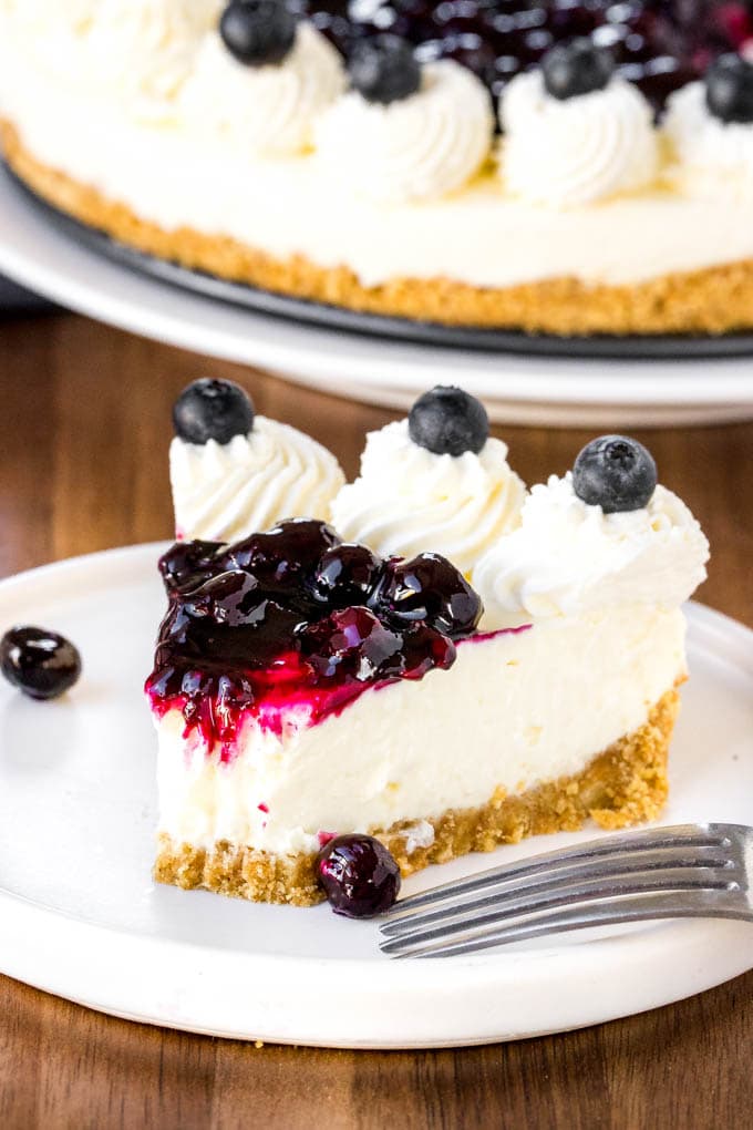 This No Bake Blueberry Cheesecake is extra creamy with a crunchy graham cracker crust and juicy blueberry topping! Perfect for summer parties and BBQs. A slice of creamy no bake blueberry cheesecake with a bite taken out of it.