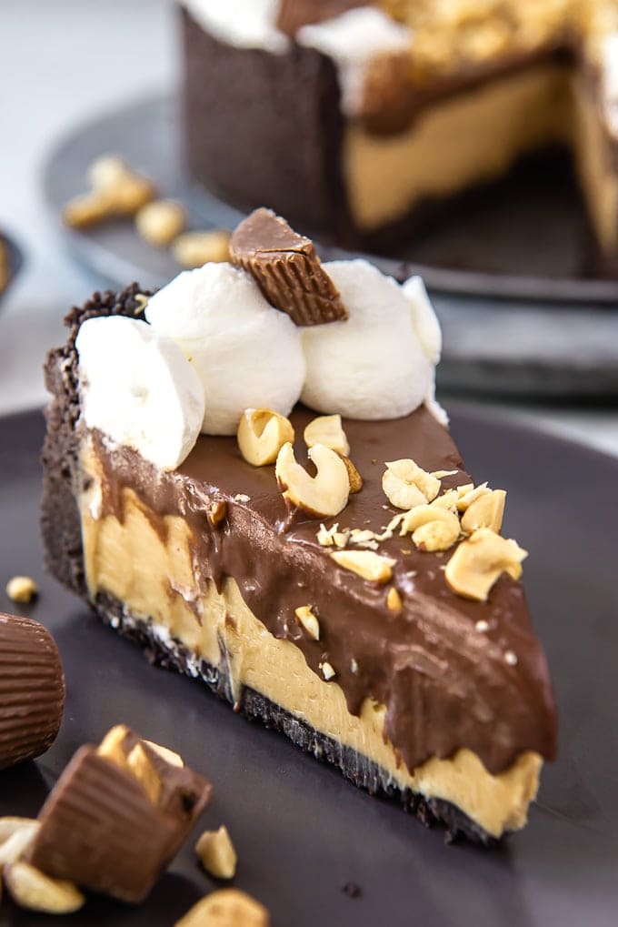 a slice of No Bake Chocolate Peanut Butter Pie with whipped cream and chopped peanuts on top on a black plate.