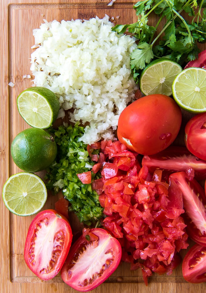 Ingredients for pico de gallo on a large cutting board.