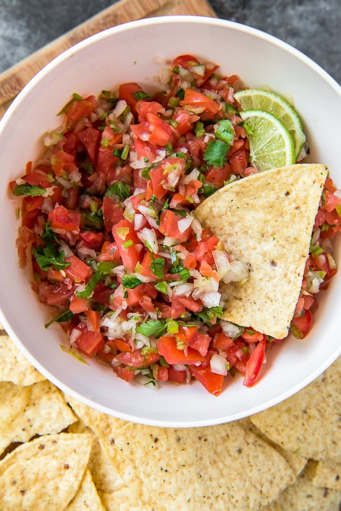 A large bowl filled with tomatoes, onions, jalapenos, cilantro and limes.