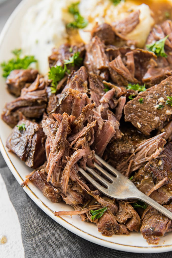 A plate of shredded beef with some on a fork.