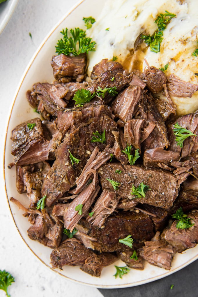 A platter of slow cooker short ribs, shredded, sitting next to mashed potatoes and gravy