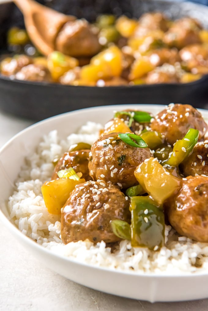 Sweet and sour meatballs with pineapple and green peppers in a bowl over rice.