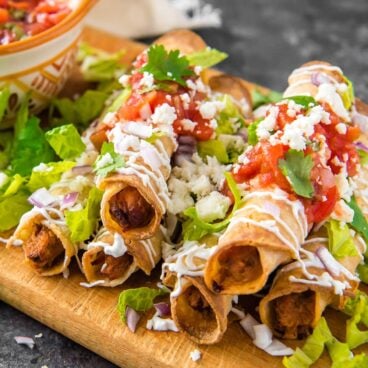 A dish is filled with Taquitos, topped with cheese, cilantro, and taco sauce.