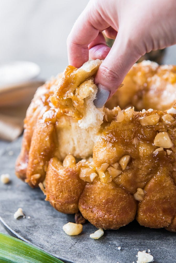 A hand reaching in and pulling a piece of monkey bread off of the loaf