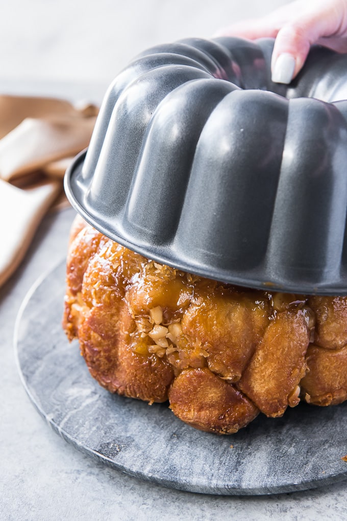 A hand lifting the bundt pan from an inverted loaf of monkey bread.