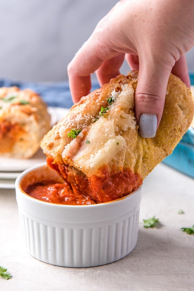 A meatball sub being dipped into a dish of marinara sauce.