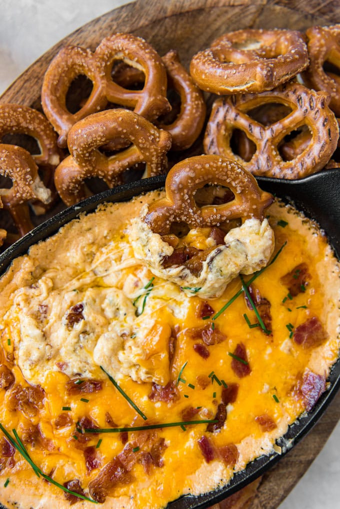 An overhead shot of a skilelt filled with baked beer cheese dip with bacon and surrounded by hard pretzels