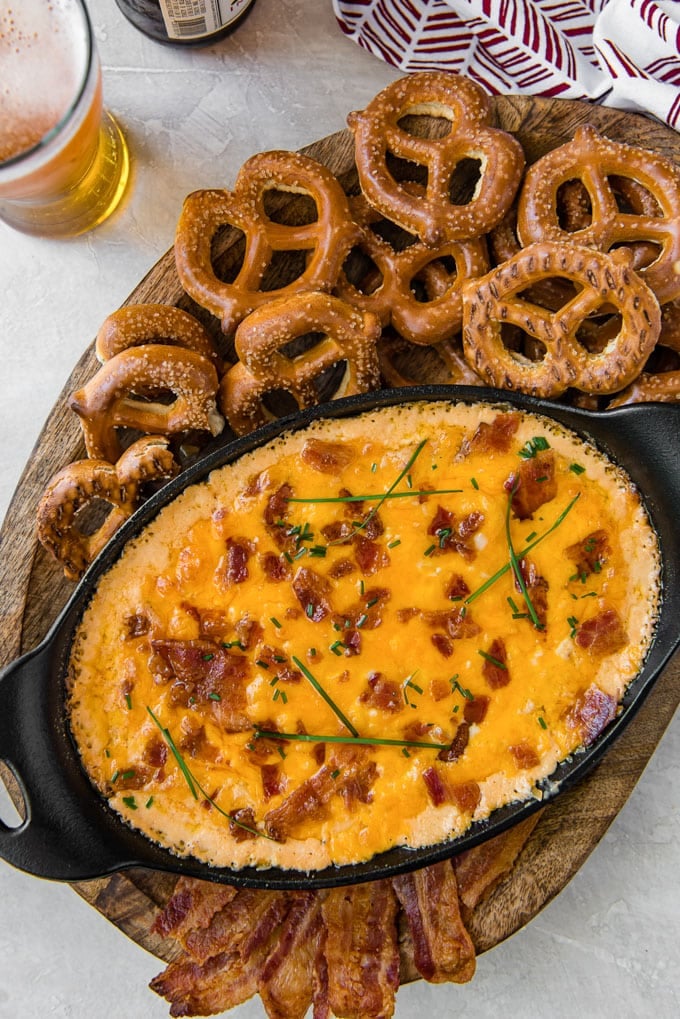 An overhead shot of a skillet of bacon beer cheese dip with pretzels and beer.