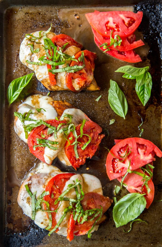 4 chicken breasts on a sheet pan topped with mozzarella, tomatoes and basil