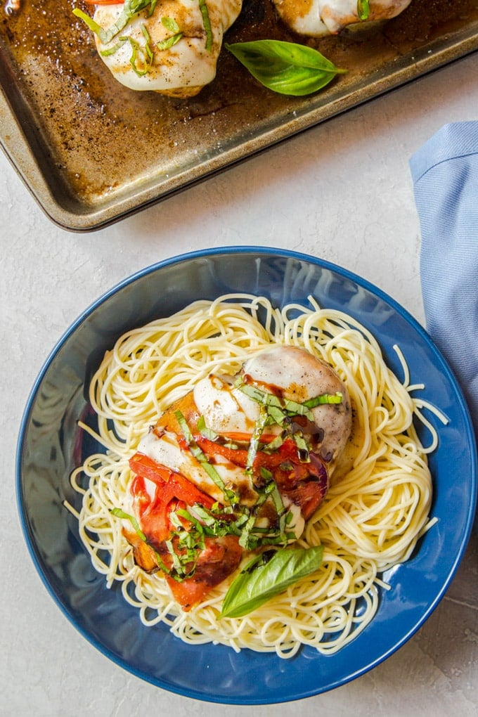 a chicken breast sitting on top of angel hair pasta with tomatoes and basil