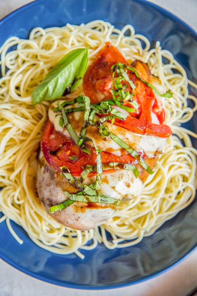 A close up image of a baked caprese chicken breast on top of angel hair pasta 