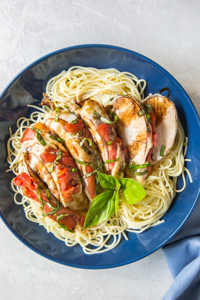 Slices of balsamic covered chicken over angel hair pasta with tomatoes and basil