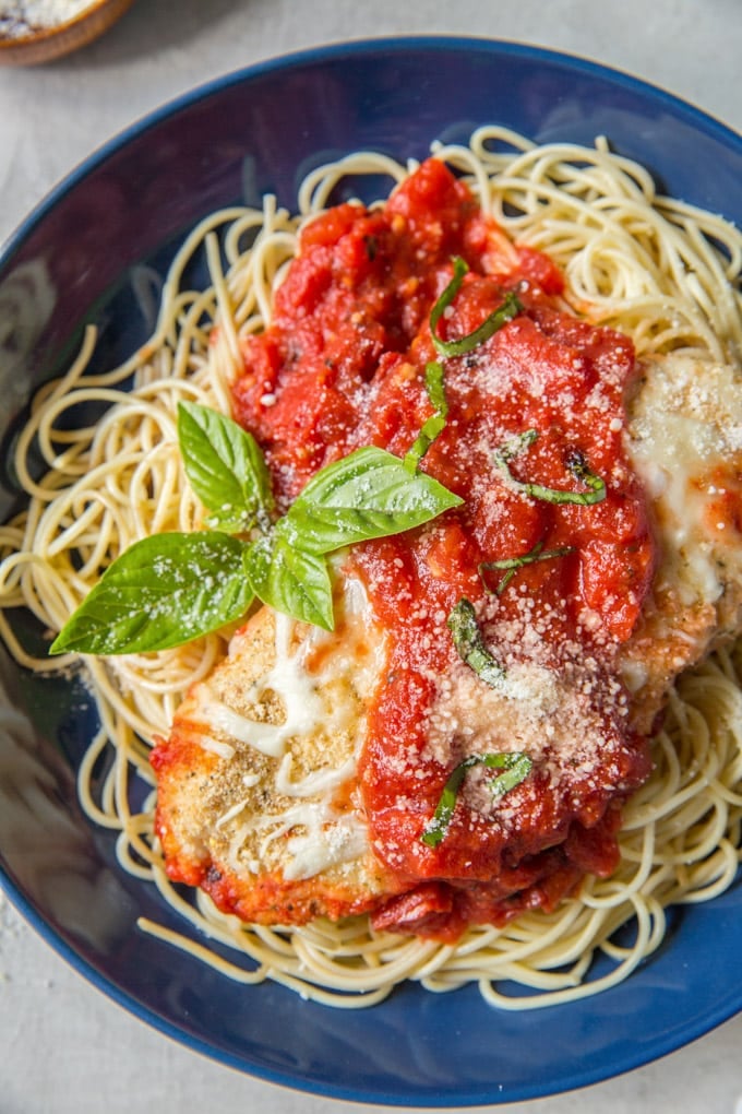 A piece of Baked Chicken Parmesan over spaghetti and topped with marinara sauce, parmesan cheese and fresh basil.