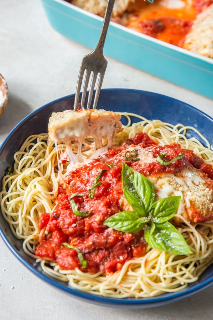 A fork taking a slice of chicken parmesan with string of melted cheese.