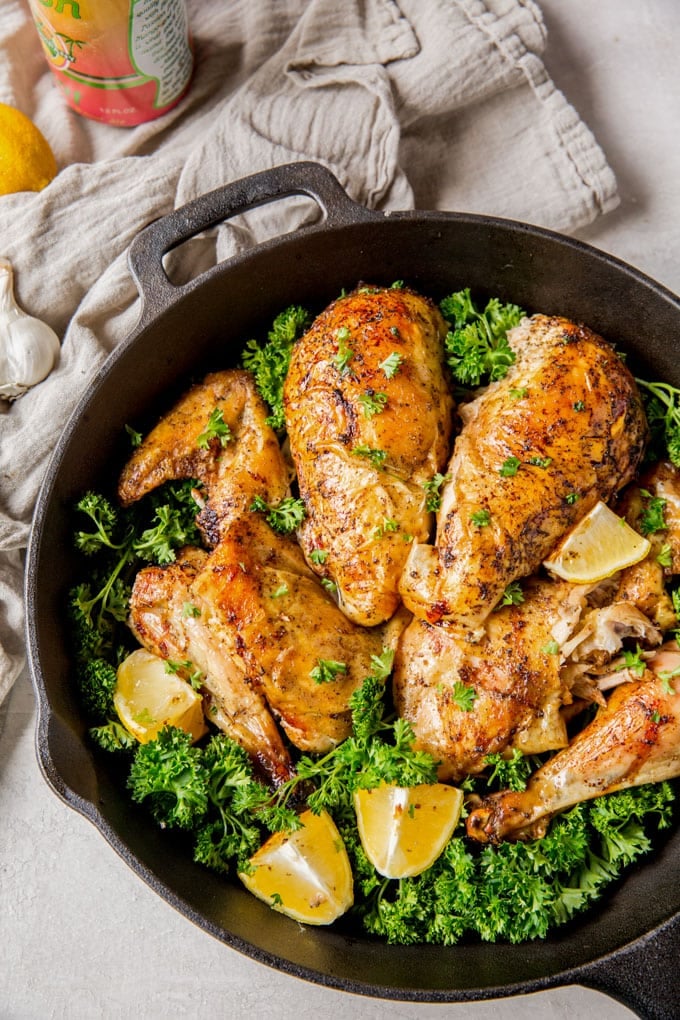 A cast iron skillet with a whole chicken cut up into quarters, with parsley and lemon