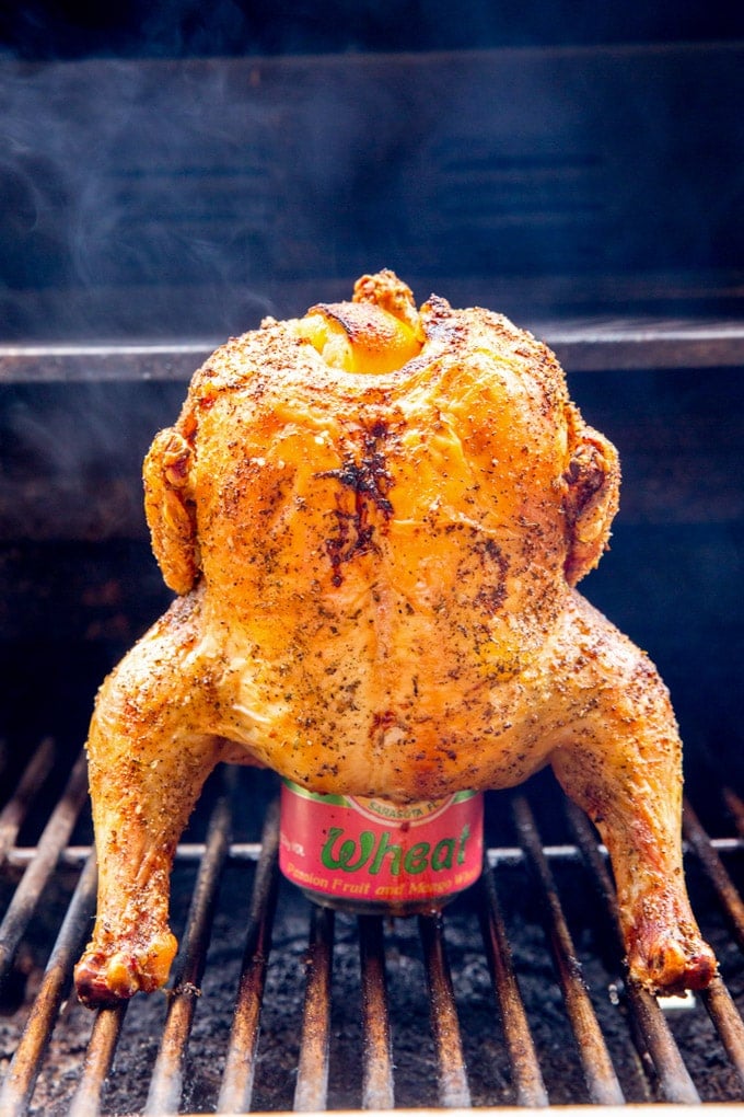 whole chicken, sitting on top of a beer can, on a bbq grill.