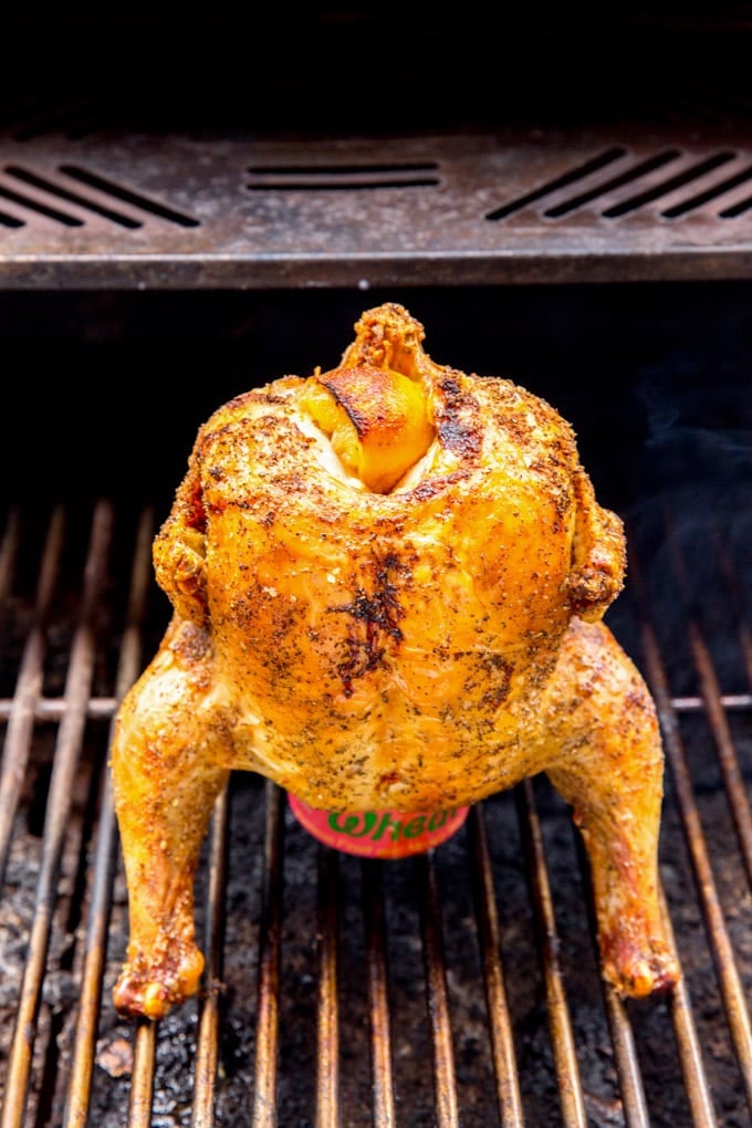 A whole chicken sitting on top of a beer can on a grill