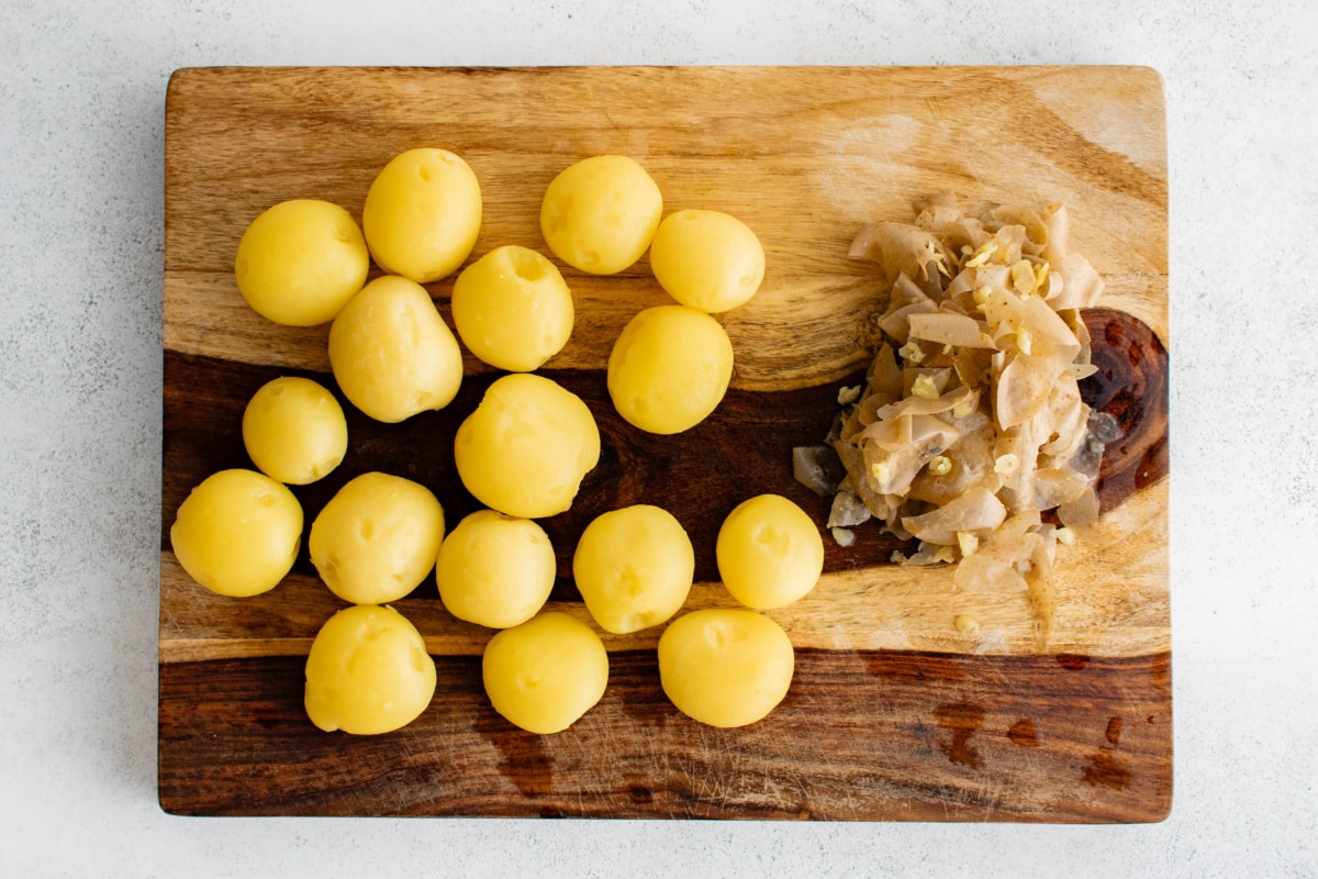 Peeled potatoes on a wood cutting board.