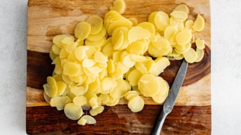 Sliced potatoes on a wood cutting board.