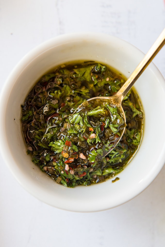 Chimichurri sauce in a white dish with a gold spoon