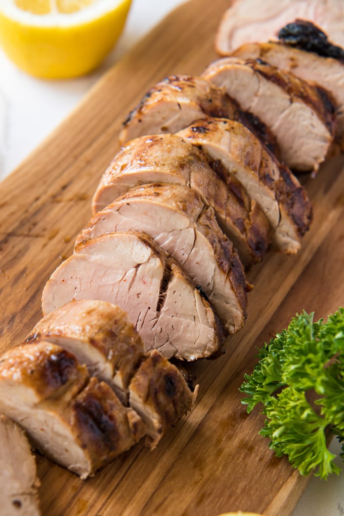 Sliced grilled pork tenderloin on a wood cutting board.