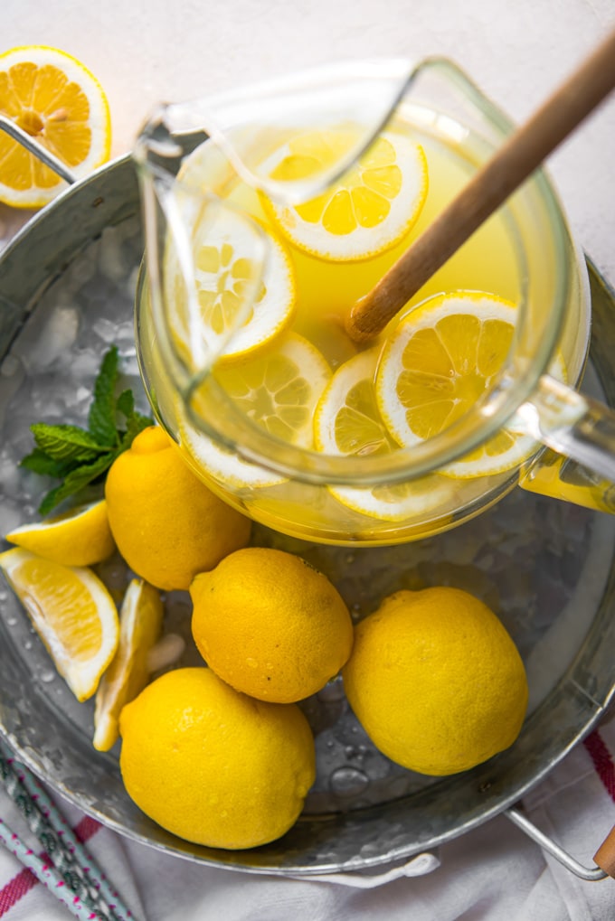 An overhead shot of a pitcher of lemonade sliced lemons and a spoon for stirring.
