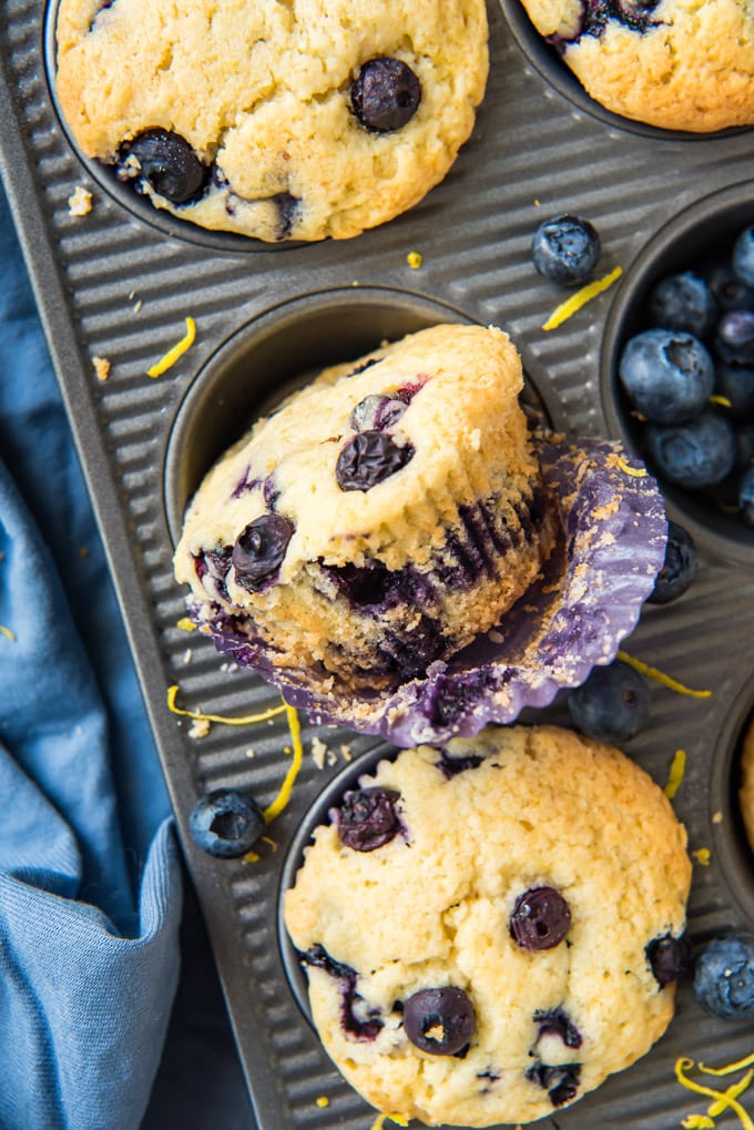 A close up of a pan of blueberry muffins with one sitting sideways