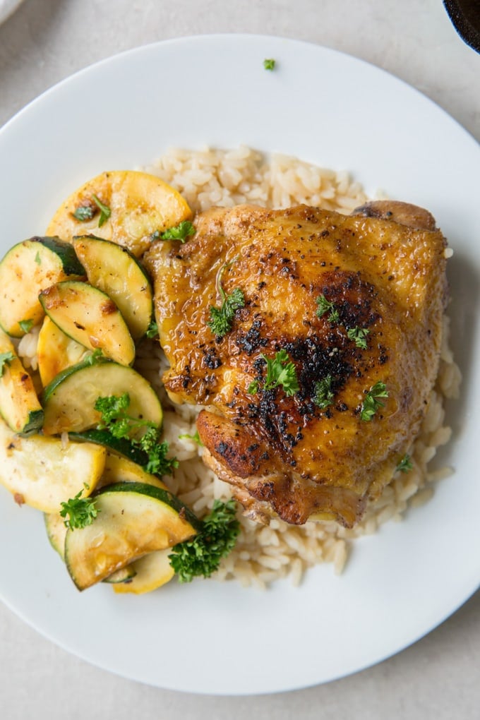 A single chicken thigh over rice with a side of zucchini