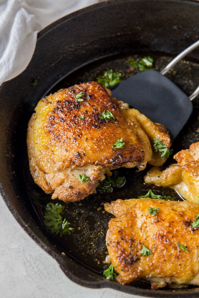Chicken thighs in a cast iron skillet, one is being lifted by a spatula.