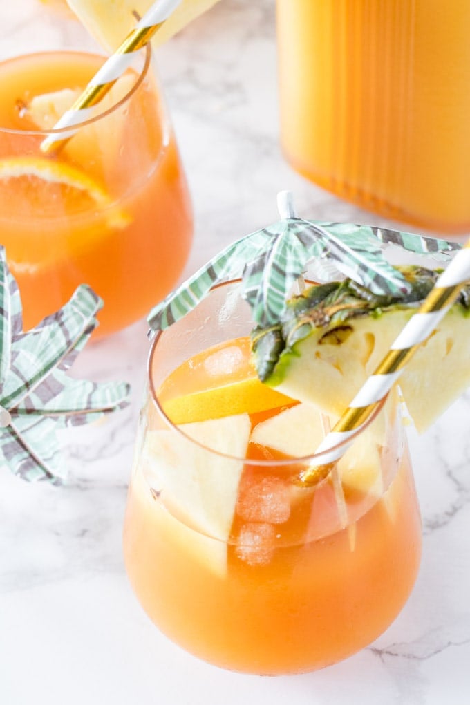 Overhead shot of a glass of rum punch with pineapple, ice cubes and orange slices in the glass. 