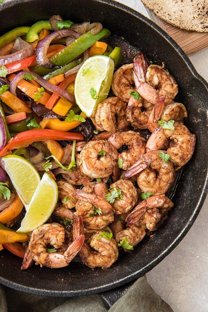 An overhead shot of shrimp, peppers, onions and limes in a skillet, ready to make shrimp fajitas