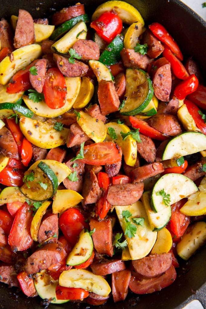 A close up image of smoked sausage and vegetables in a cast iron skillet.