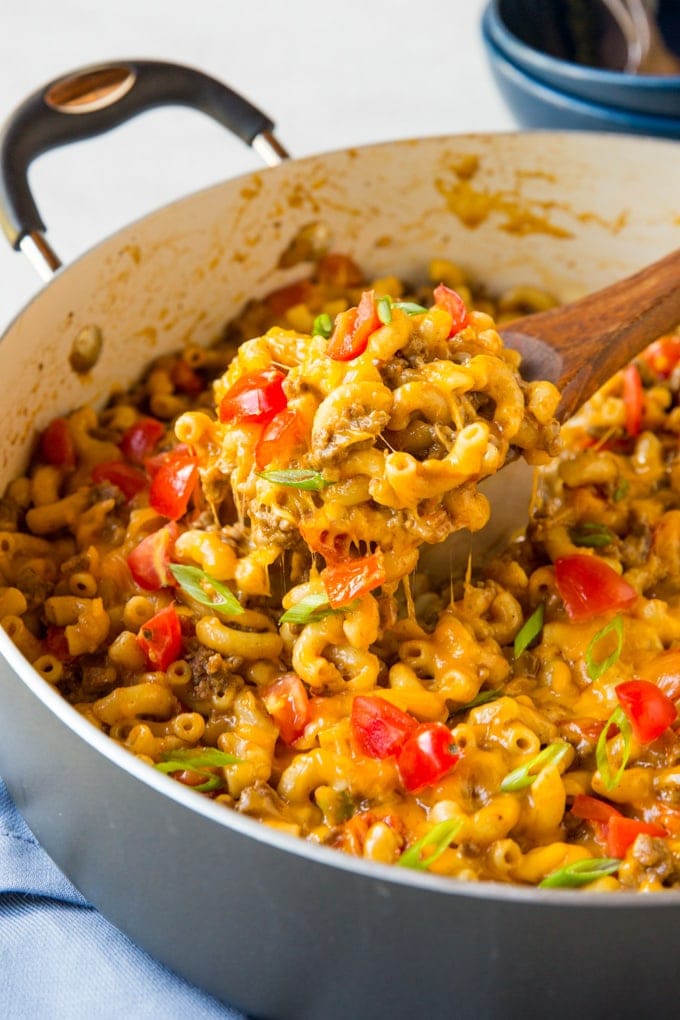 A large pot with taco mac and cheese. A wooden spoon lifts a serving up