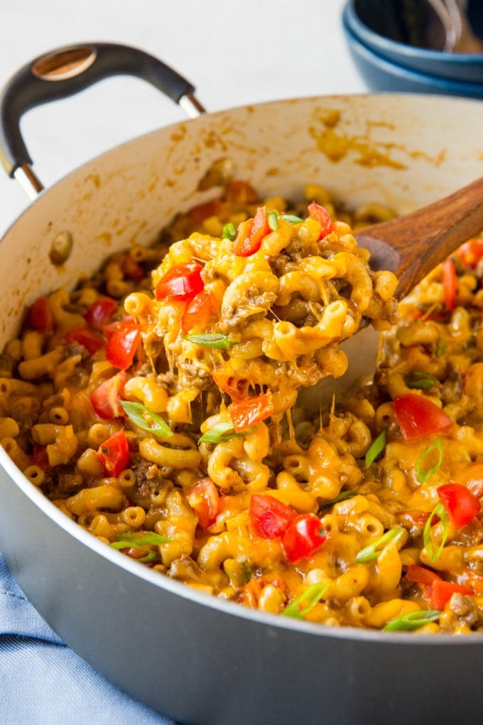 A large pot with taco mac and cheese. A wooden spoon lifts a serving up 