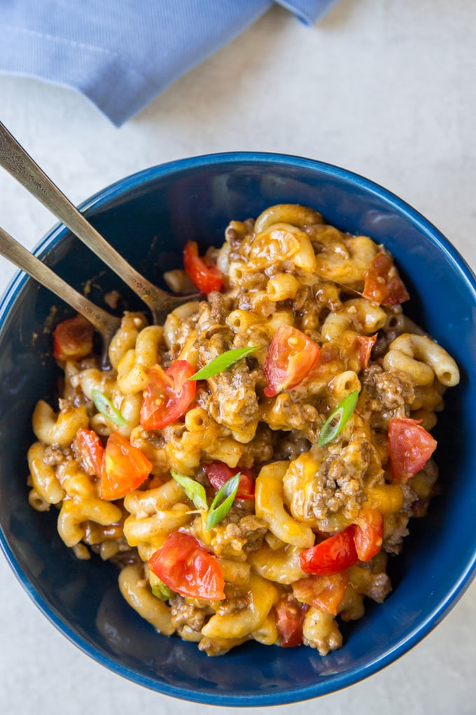 A bowl of cheesy taco macaroni with two forks and sliced green onion garnish