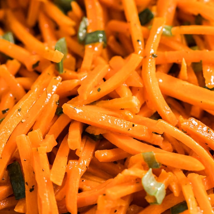 A close up image of shredded carrots and green onions.