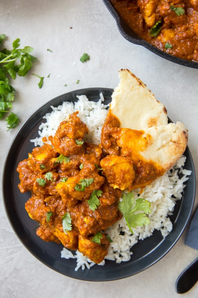 A blue plate with white rice, chicken curry and naan bread. Topped with cilantro.