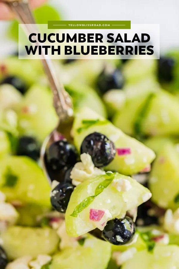 A pinterest friendly image of cucumber salad with blueberries on a spoon. Image includes title text overlay.