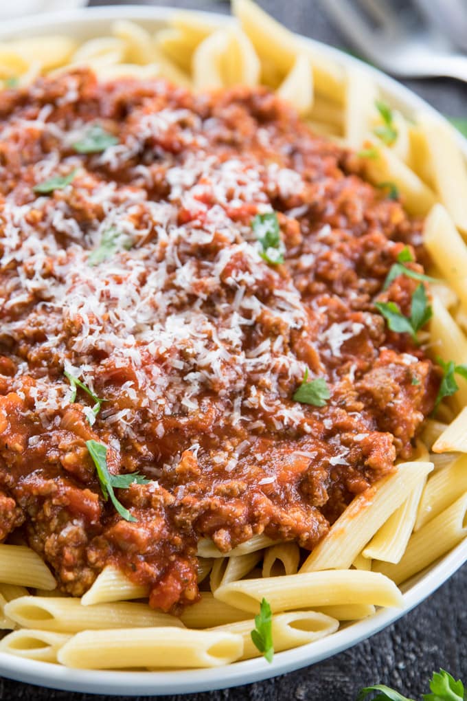 A close up image of penne pasta with bolognese meat sauce